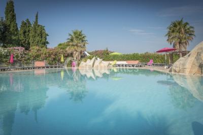 Des animatrices en jupes hawaïennes dansent devant un groupe d'enfants et d'adultes près d'une piscine extérieure.
