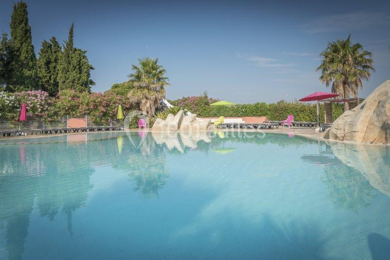 Piscine extérieure entourée de végétation, avec chaises colorées, parasols et ciel dégagé en arrière-plan.