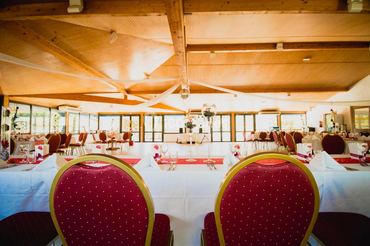 Salle de réception lumineuse avec tables dressées, chaises rouges et plafond en bois.