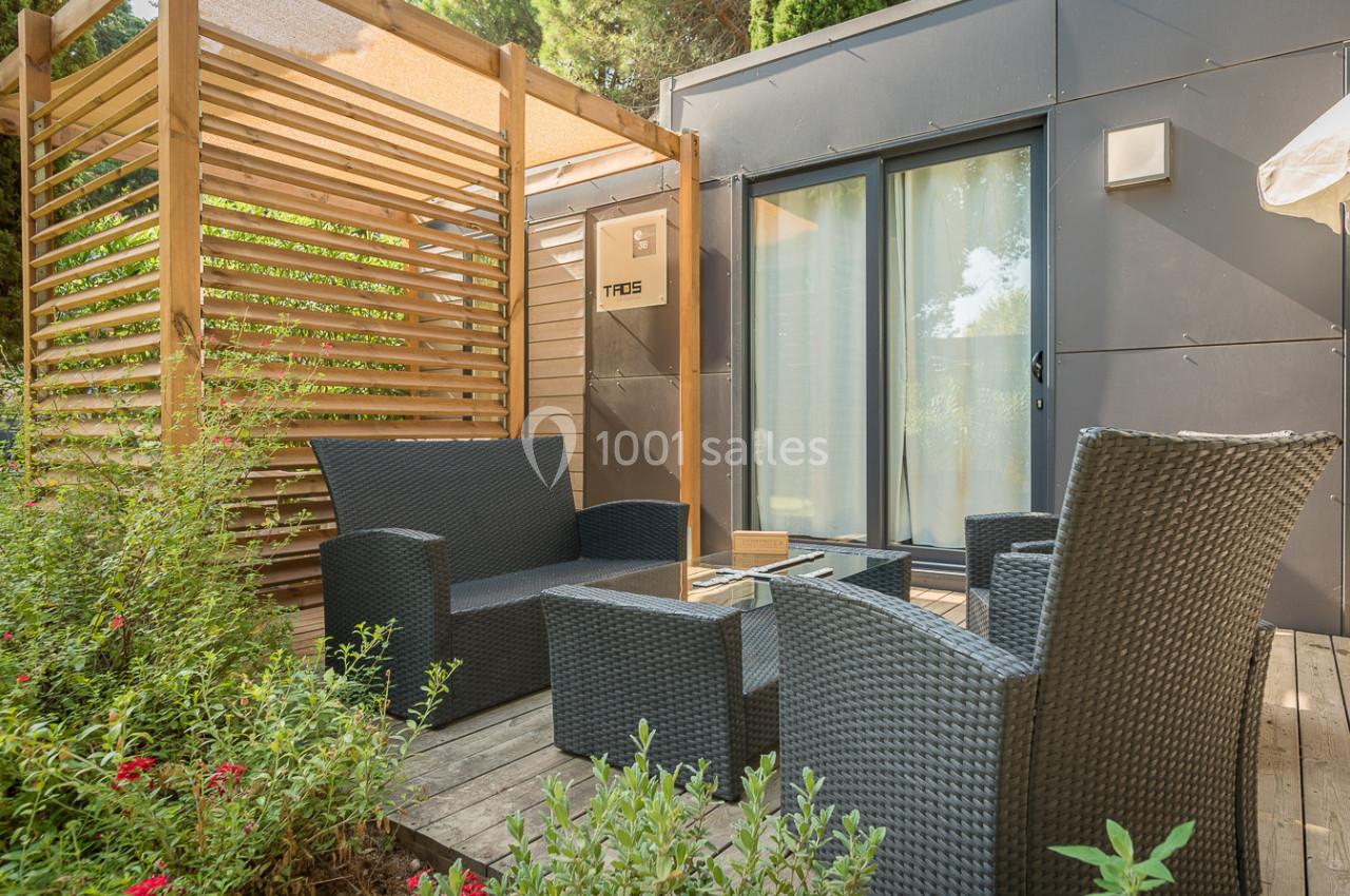 Mobilier de jardin en résine tressée sur une terrasse en bois, entourée de végétation et attenante à un logement moderne.