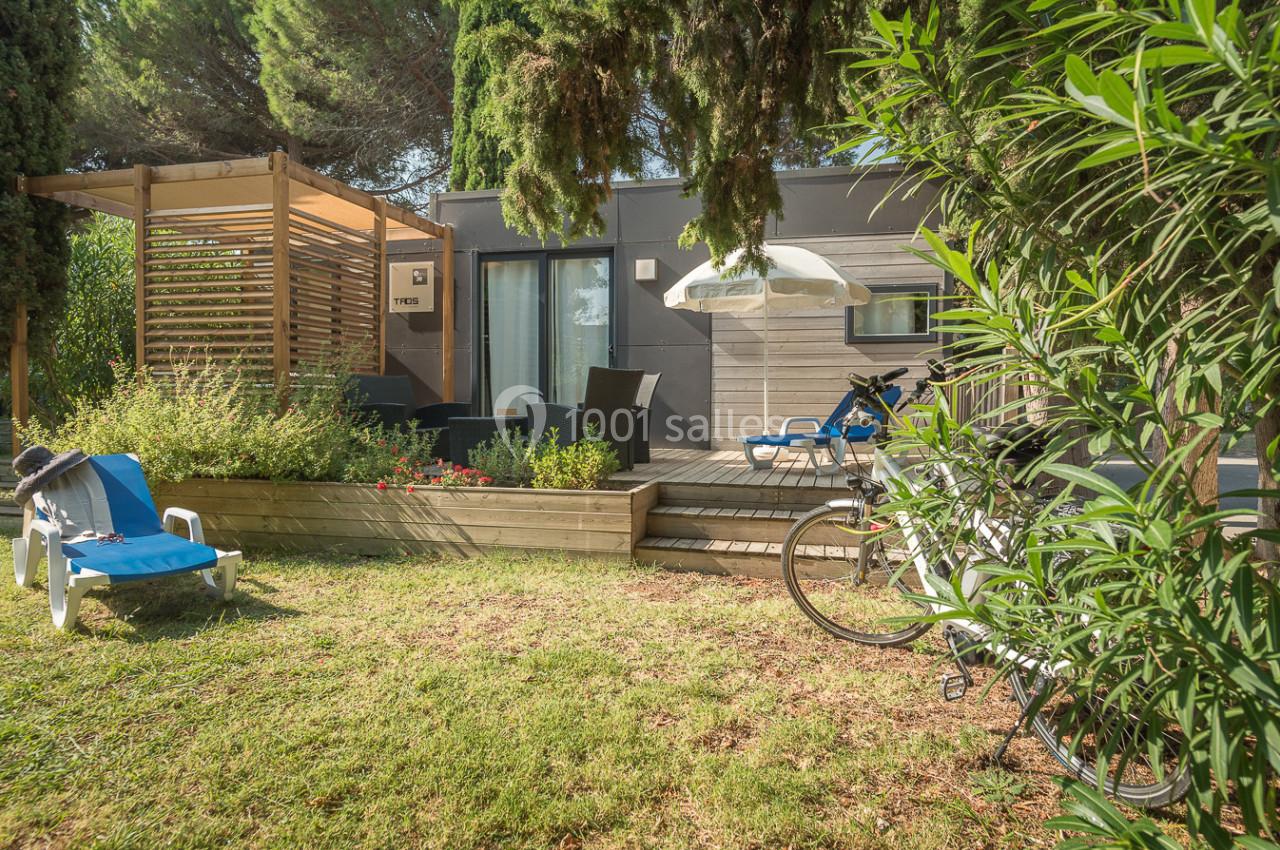 Espace extérieur avec terrasse en bois, chaises longues, vélos et végétation entourant une habitation moderne.