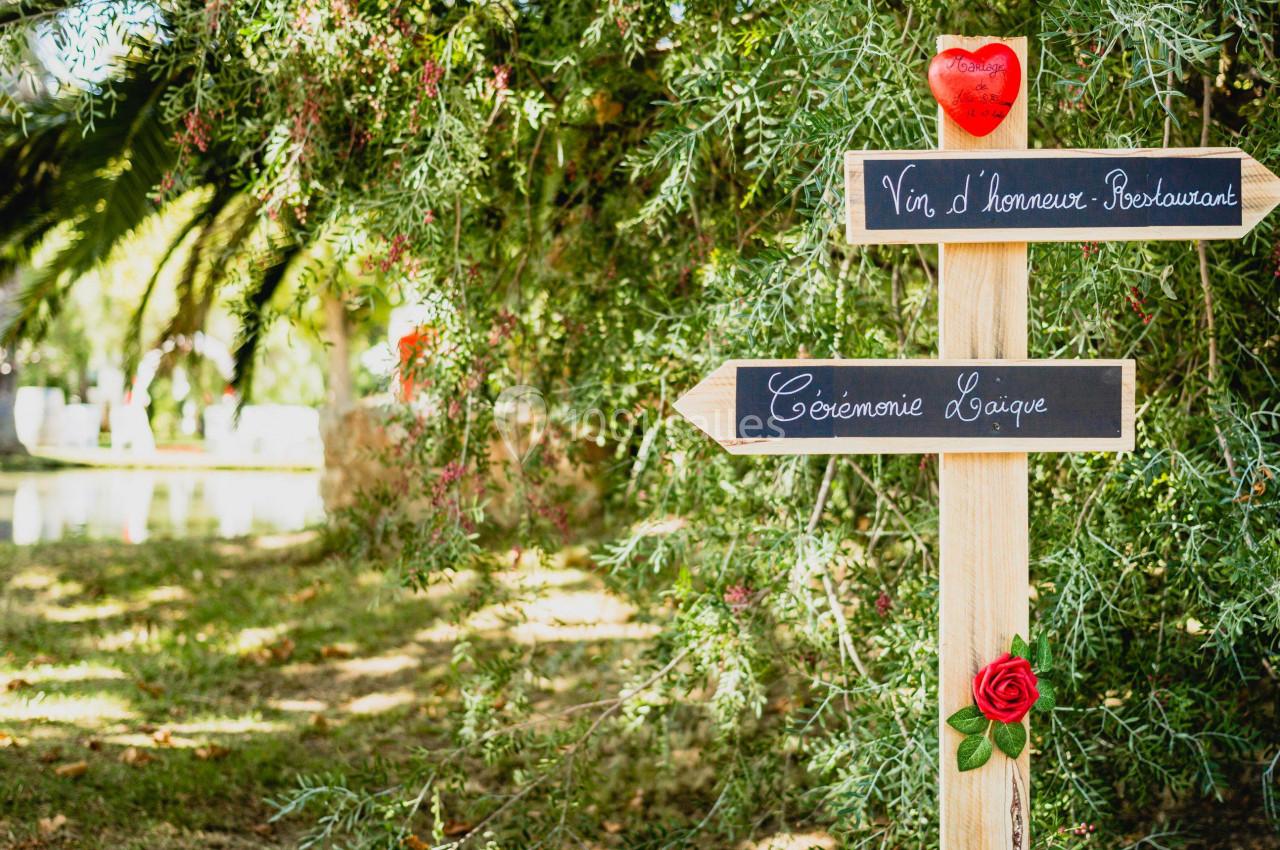 Panneaux en bois indiquant ’Vin d'honneur - Restaurant’ et ’Cérémonie laïque’, décorés de fleurs et d'un cœur rouge.