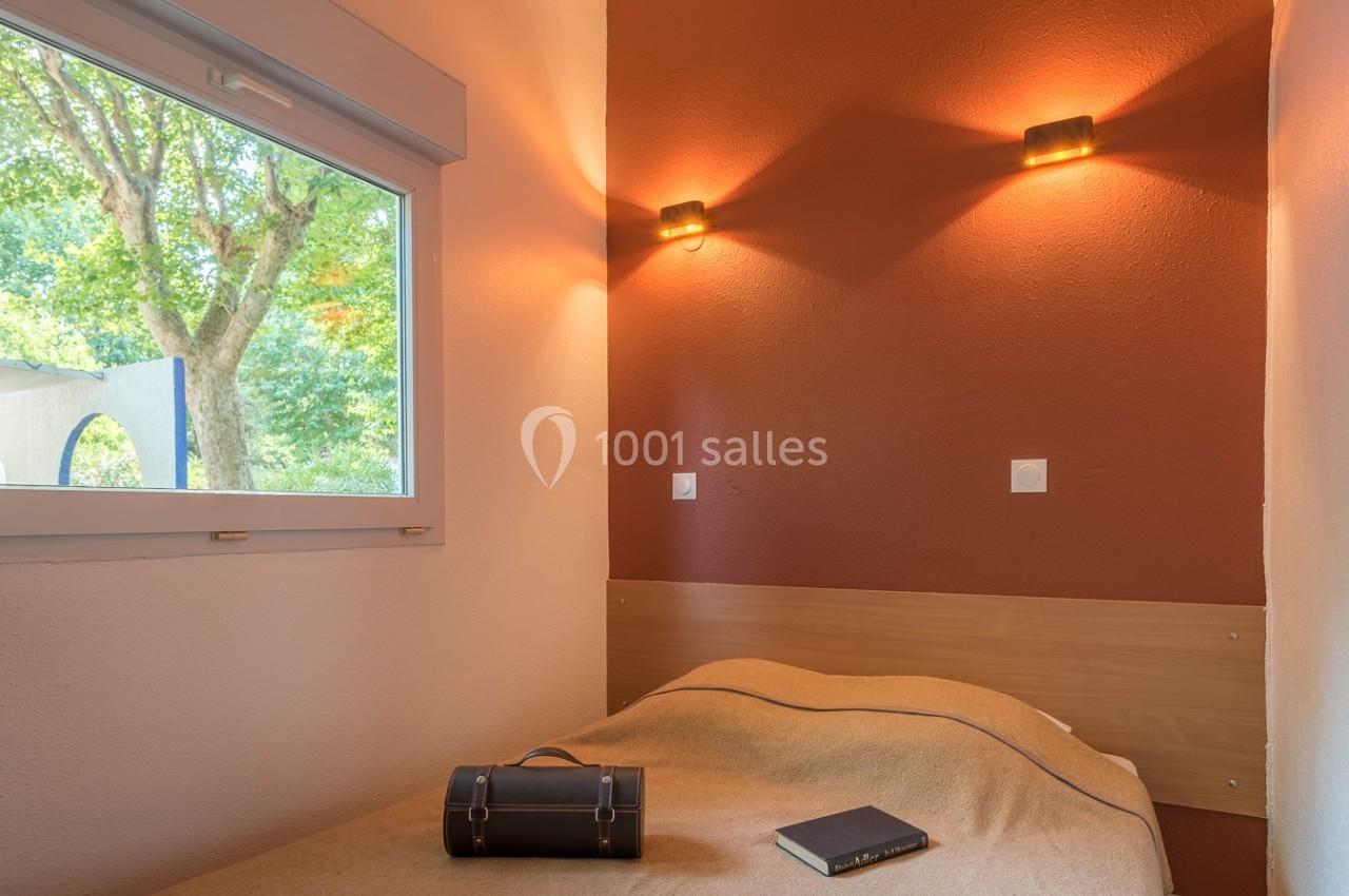 Chambre simple avec un lit, une fenêtre donnant sur un arbre, un livre et une valise posés sur la couverture.