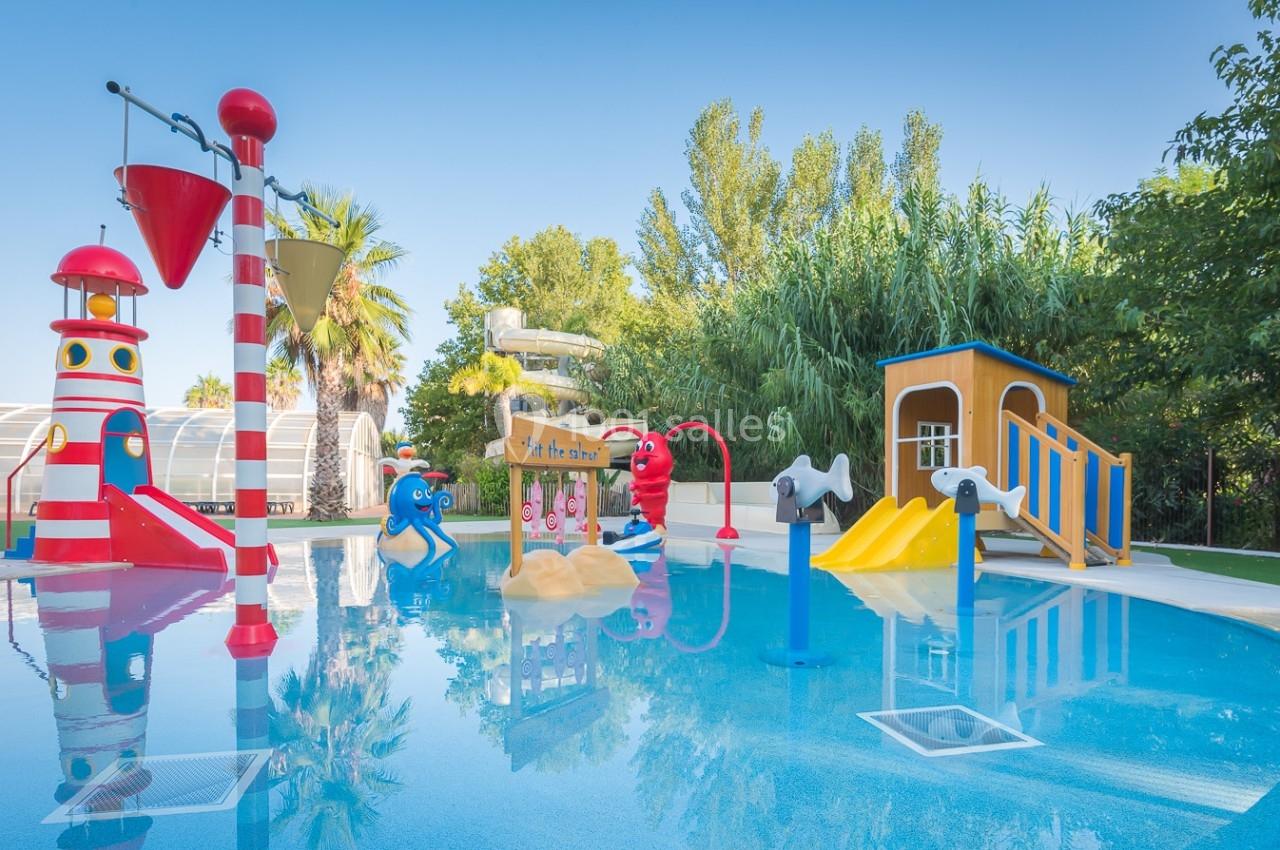 Aire de jeux aquatique pour enfants avec toboggans colorés, jets d'eau et structures ludiques entourée de végétation.