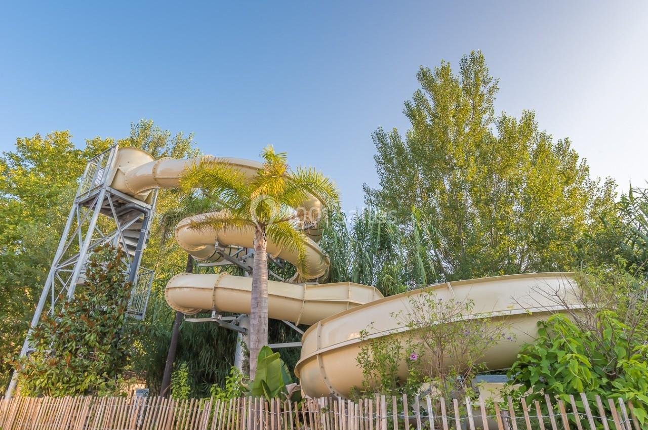 Toboggan aquatique en spirale entouré de végétation et clôturé, sous un ciel dégagé.