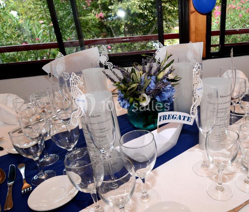 Table décorée pour un événement avec nappes bleues et blanches, verres, menus et centre de table floral bleu.
