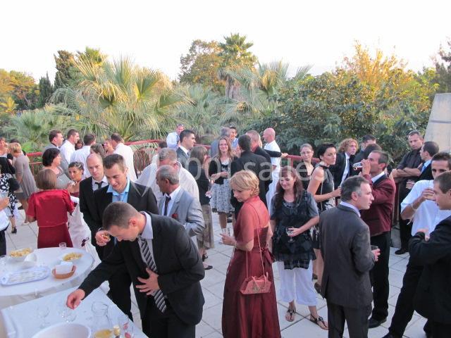 Groupe de personnes rassemblées sur une terrasse extérieure lors d'un événement, entourées de végétation.