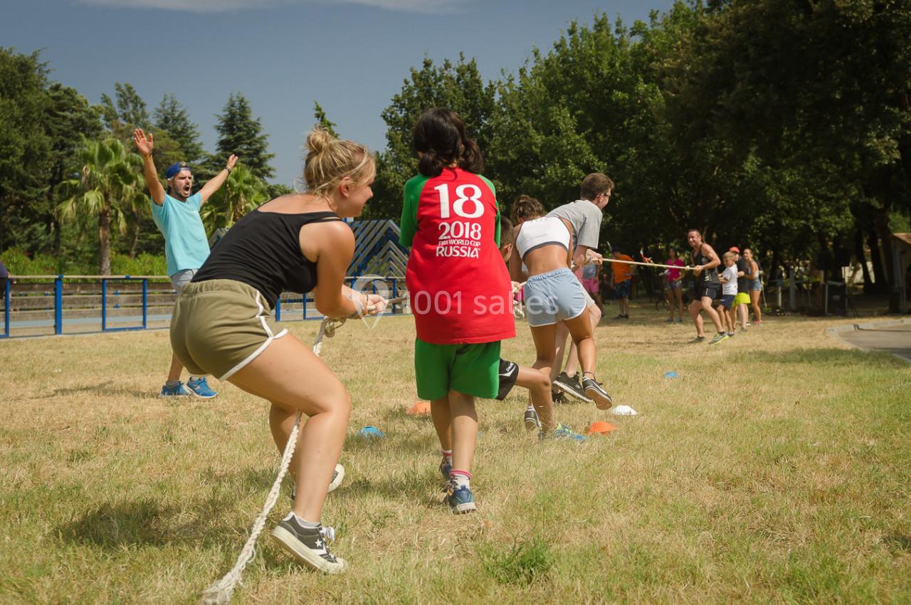 Des personnes participent à un jeu de tir à la corde en plein air sur une pelouse, sous un ciel dégagé.