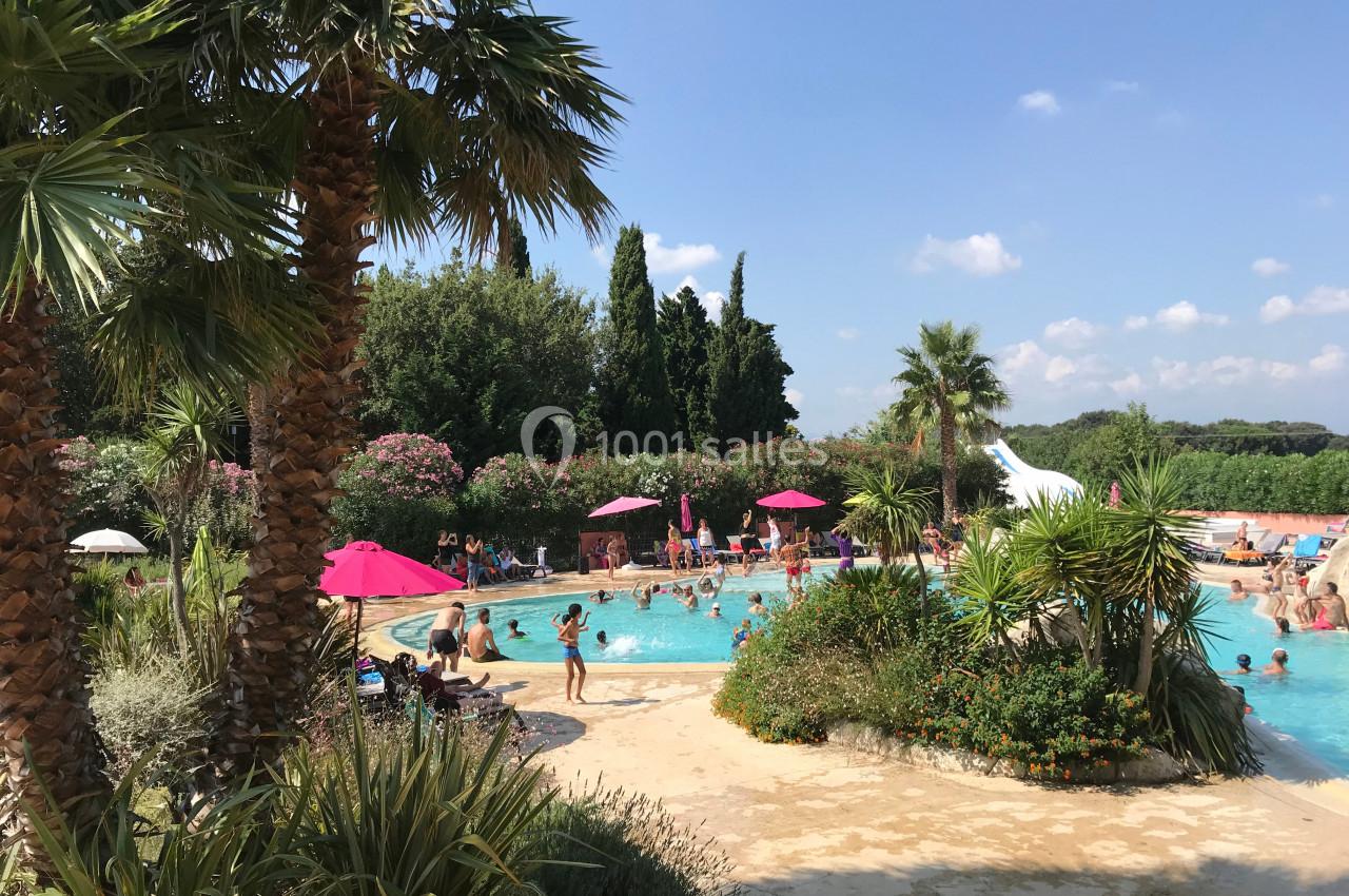 Piscine extérieure entourée de palmiers et de végétation, avec des personnes profitant du soleil et de l'eau.