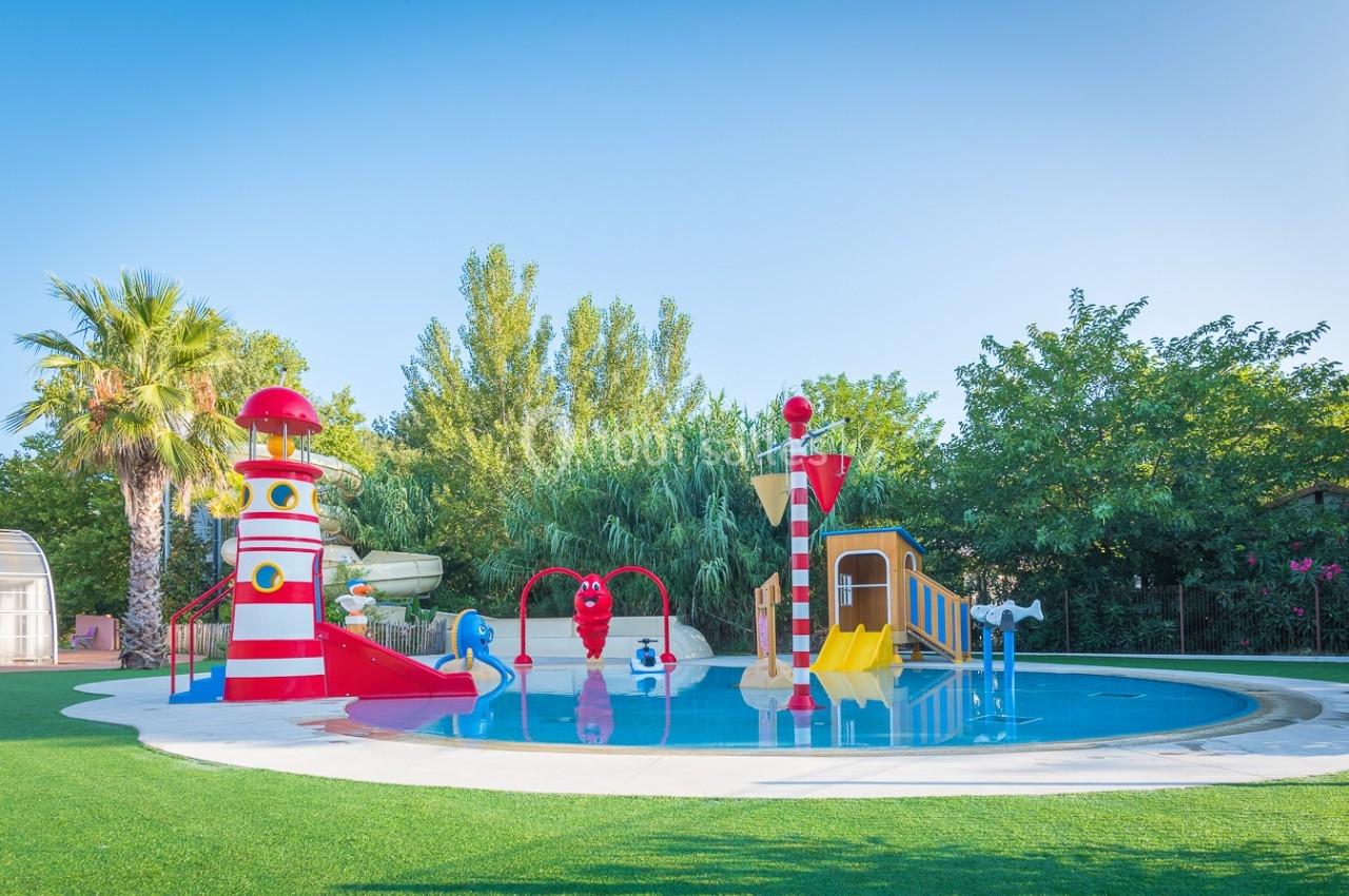 Aire de jeux aquatique avec toboggans colorés, jets d'eau et décorations en forme de phare, entourée de verdure.