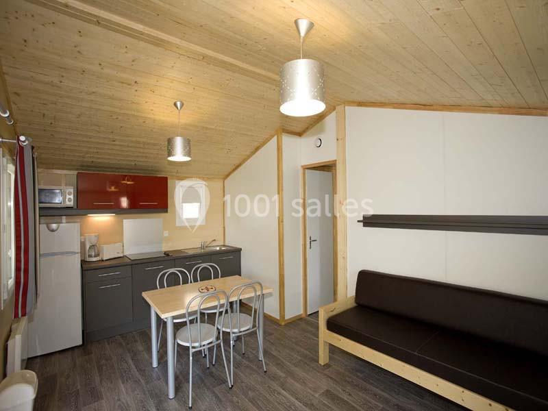 Intérieur d'un petit chalet avec cuisine équipée, table à manger, canapé et éclairage suspendu.