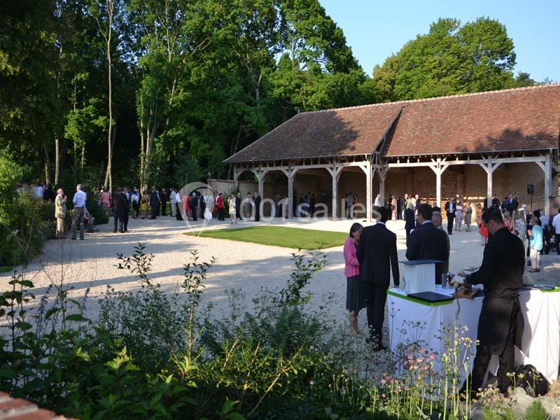 Groupe de personnes rassemblées dans une cour extérieure devant un bâtiment en pierre avec toit en tuiles.