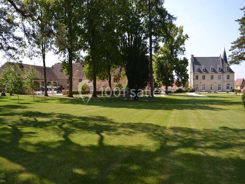 Grand jardin verdoyant avec pelouse, arbres imposants et bâtiments anciens en pierre en arrière-plan.
