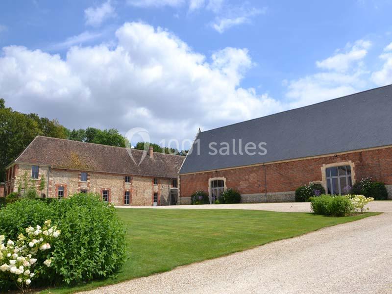 Bâtiments en briques et pierre avec toits en ardoise entourés de pelouses et arbustes sous un ciel partiellement nuageux.