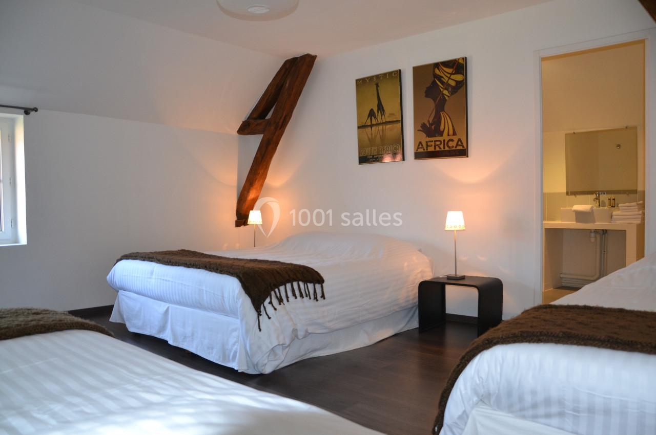 Chambre lumineuse avec trois lits, poutre apparente, affiches murales et salle de bain attenante visible.