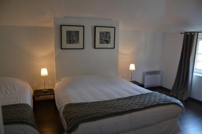 Chambre avec un lit double, un lit simple, deux lampes de chevet allumées et une fenêtre avec rideaux gris.