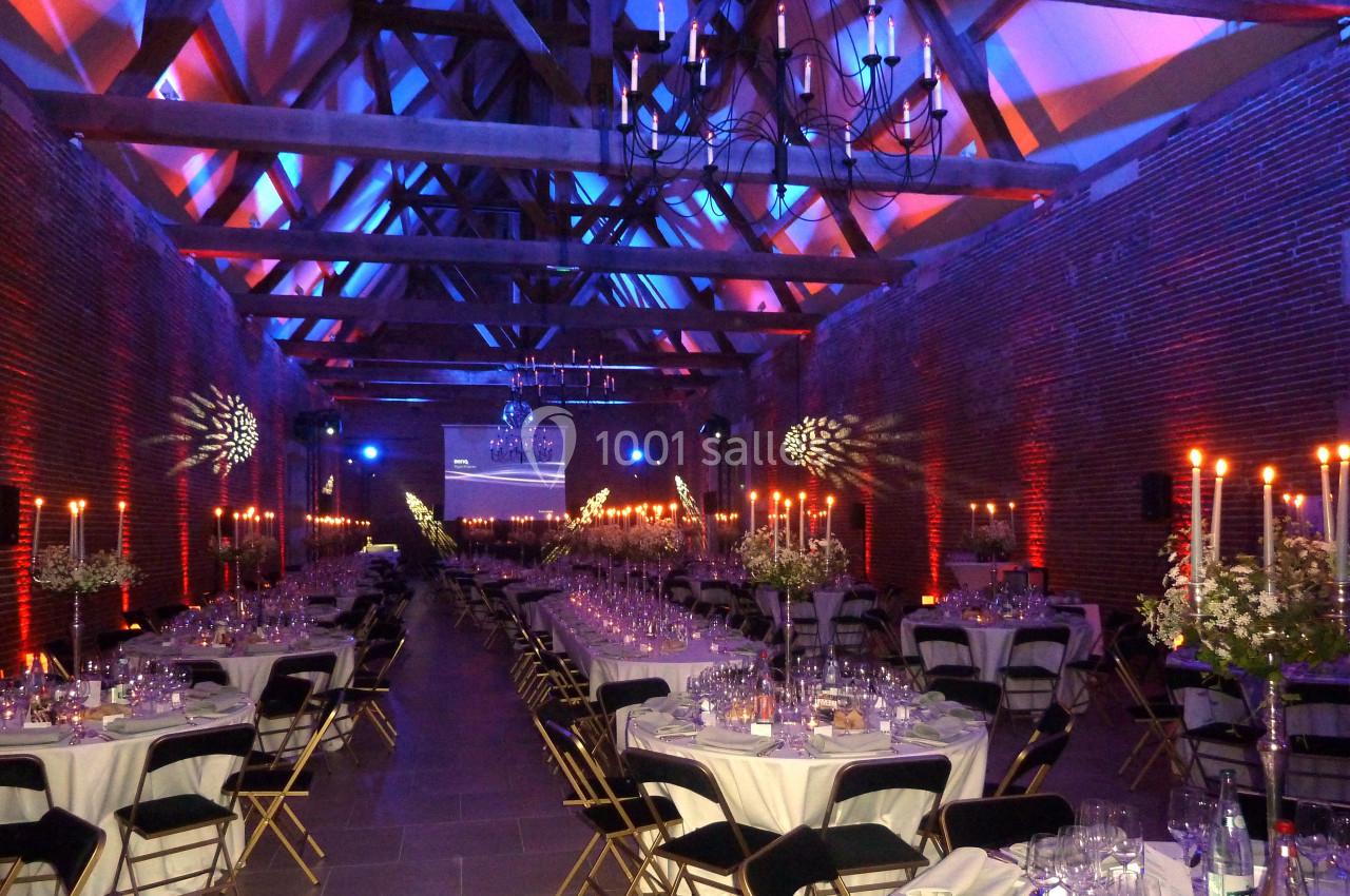 Salle de réception décorée avec des tables dressées, chandeliers allumés et éclairage coloré sur les murs en briques.