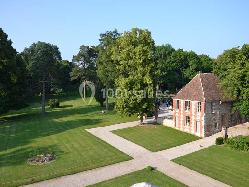 Vue d'un parc arboré avec pelouses bien entretenues, chemins en gravier et un bâtiment en briques à toit en pente.