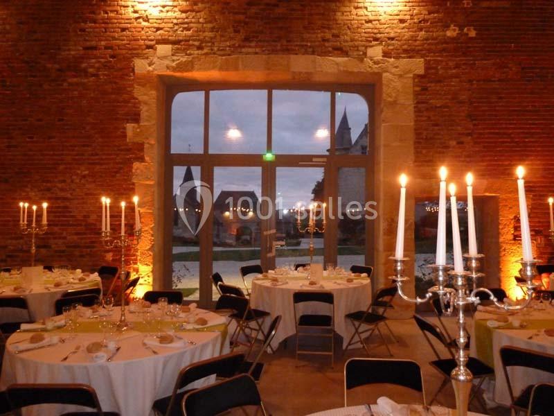Salle de réception éclairée par des chandeliers, avec des tables dressées et une vue sur un extérieur au crépuscule.