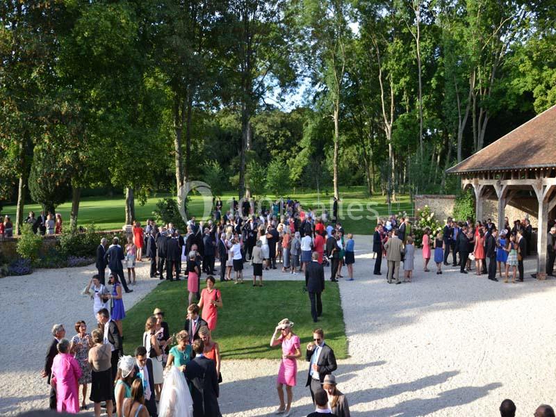 Groupe de personnes rassemblées dans un jardin lors d'un événement en plein air, entouré d'arbres et d'une structure en bois.