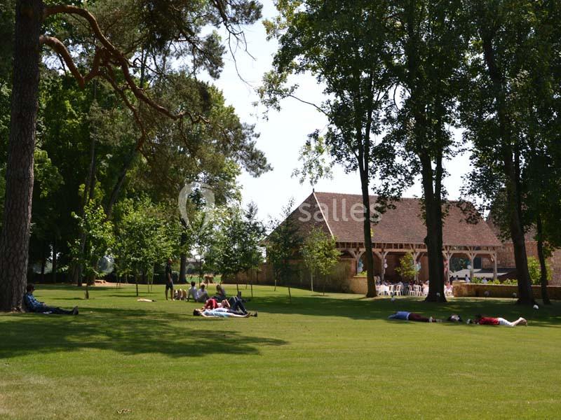 Des personnes allongées ou assises sur une pelouse ombragée près d'un bâtiment en bois entouré d'arbres.