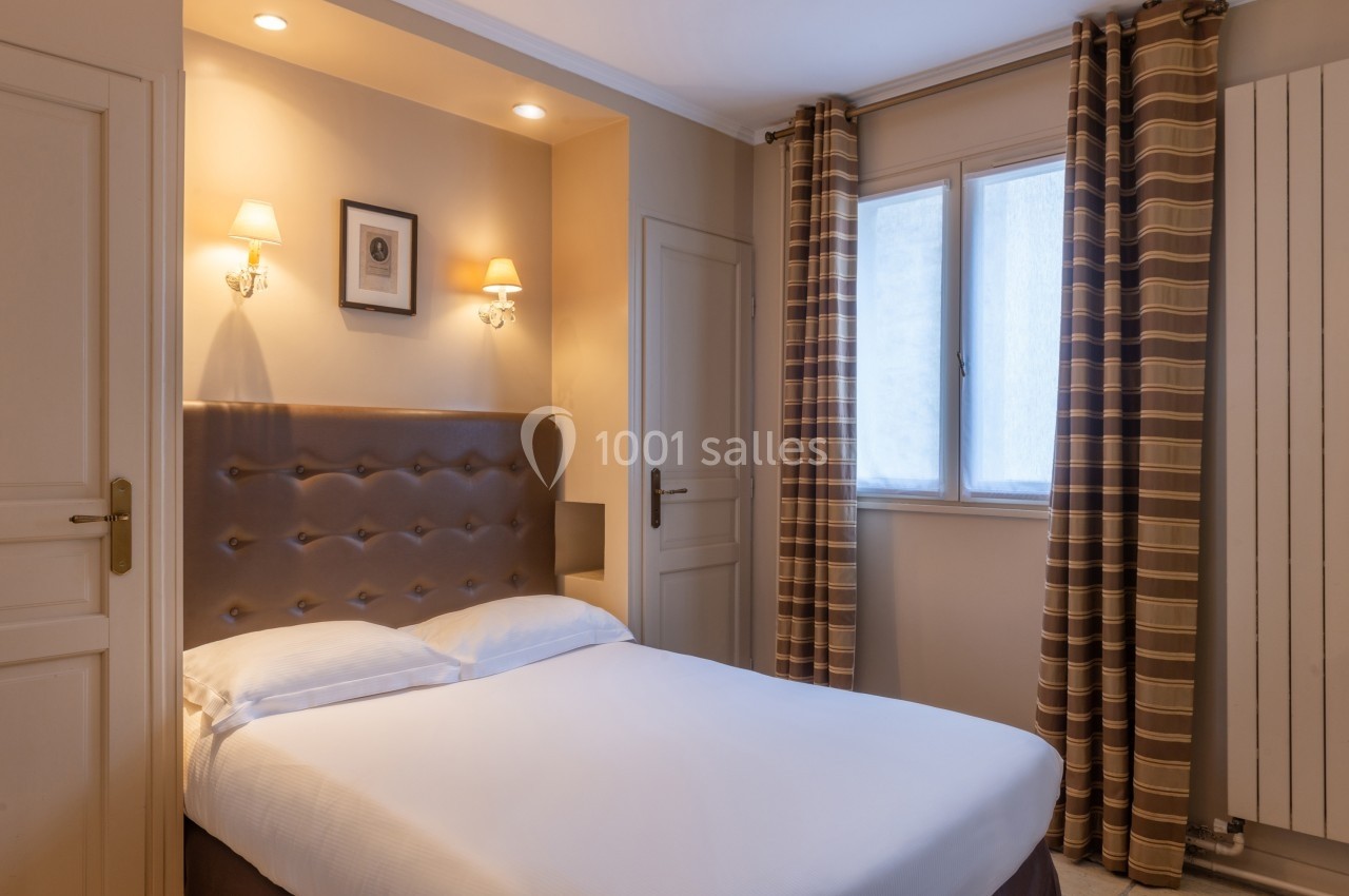 Chambre lumineuse avec un lit double, des murs clairs, des rideaux à rayures et des appliques murales allumées.