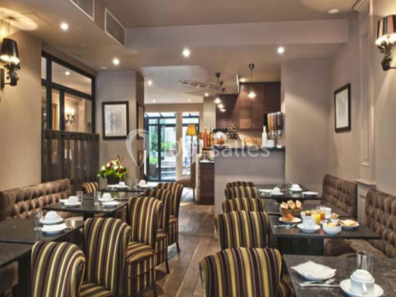 Salle de restaurant lumineuse avec tables dressées, chaises rayées et vue sur un comptoir et une baie vitrée.