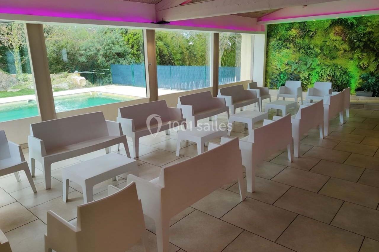 Salle lumineuse avec des bancs blancs alignés, vue sur une piscine et un mur végétal en arrière-plan.