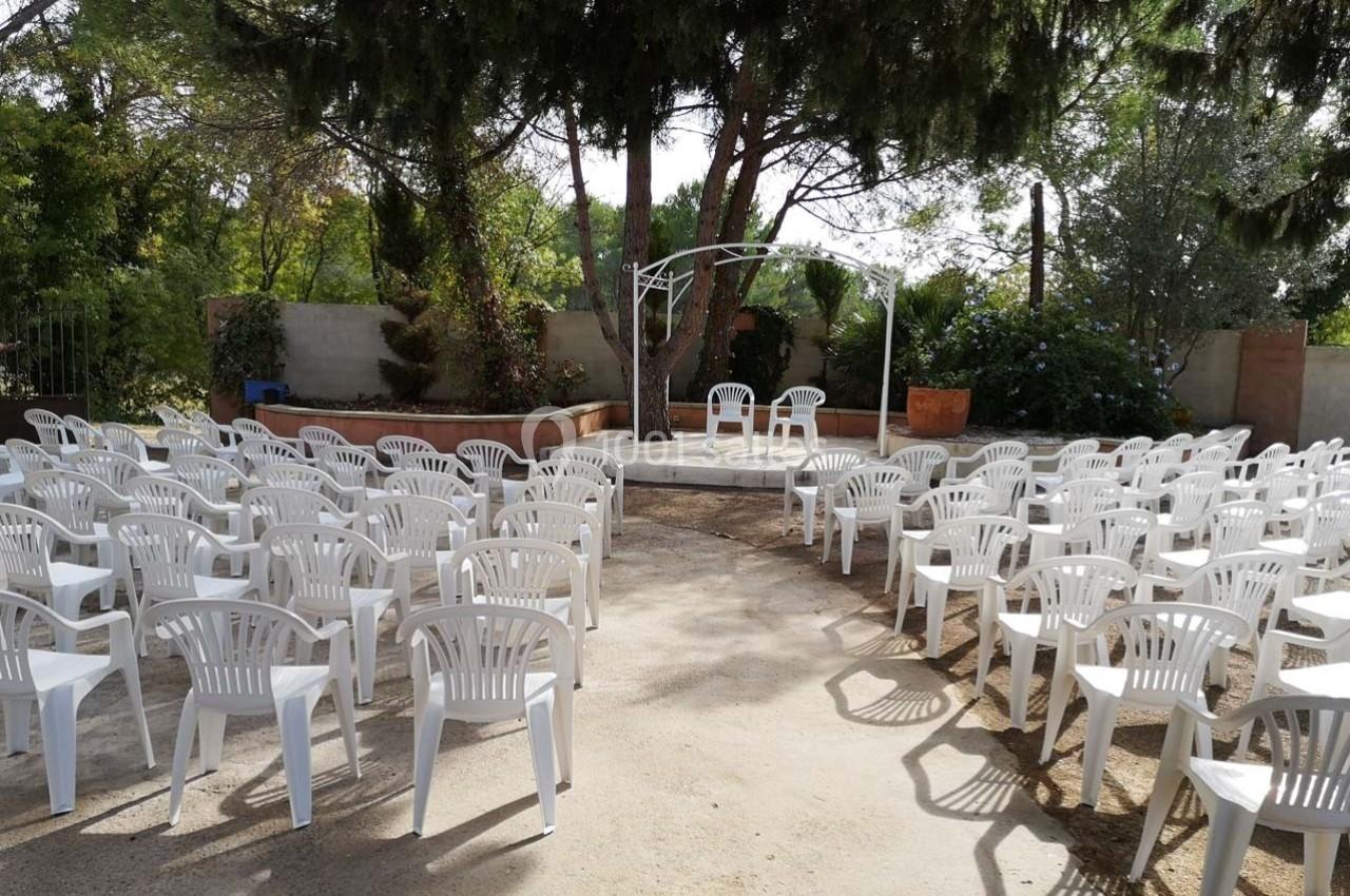 Chaises blanches disposées en rangées face à une arche décorative dans un espace extérieur entouré de verdure.