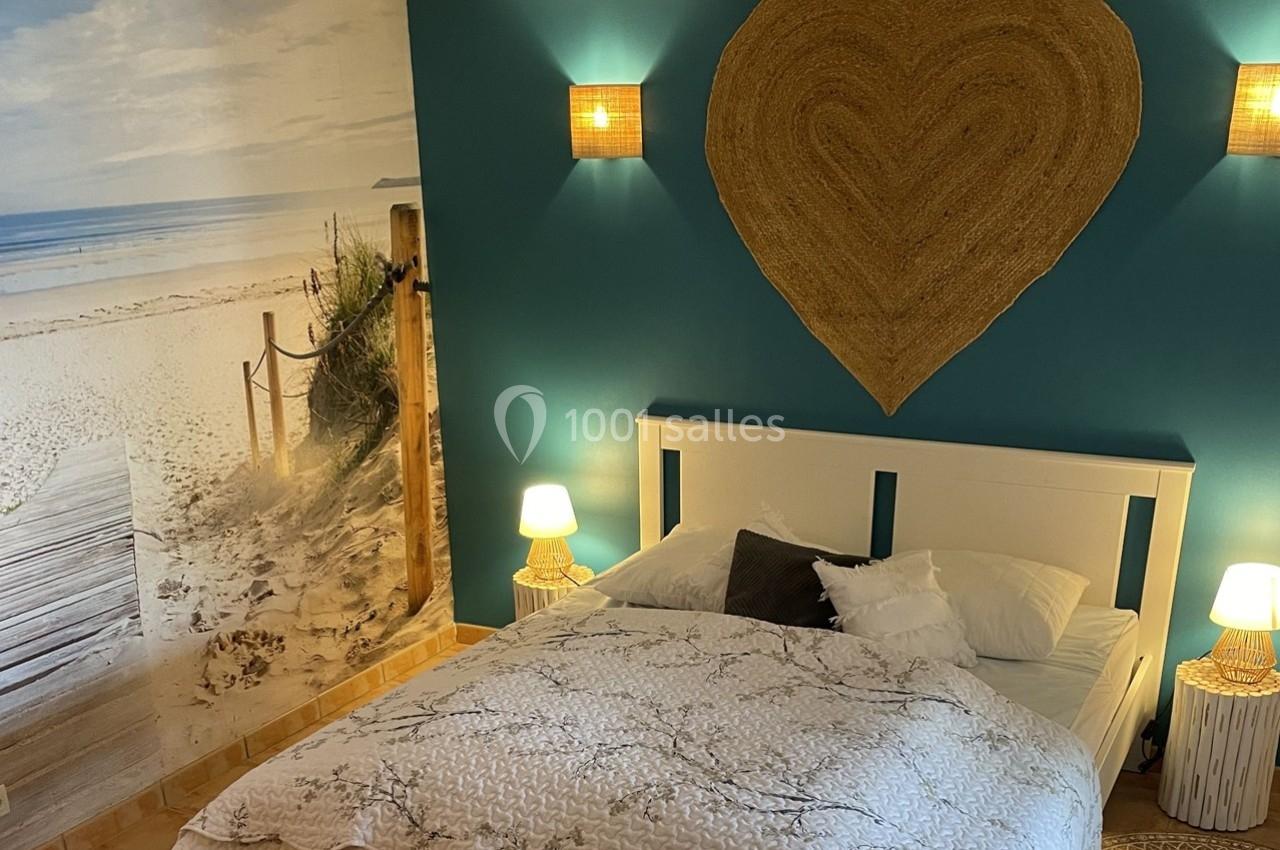 Chambre avec un lit double, mur bleu décoré d'un cœur en osier et fresque murale représentant une plage.