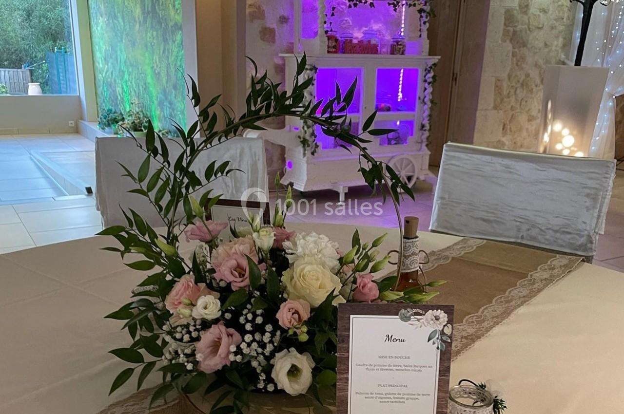 Centre de table floral avec roses et feuillage, menu posé à côté, dans une salle décorée pour un événement.