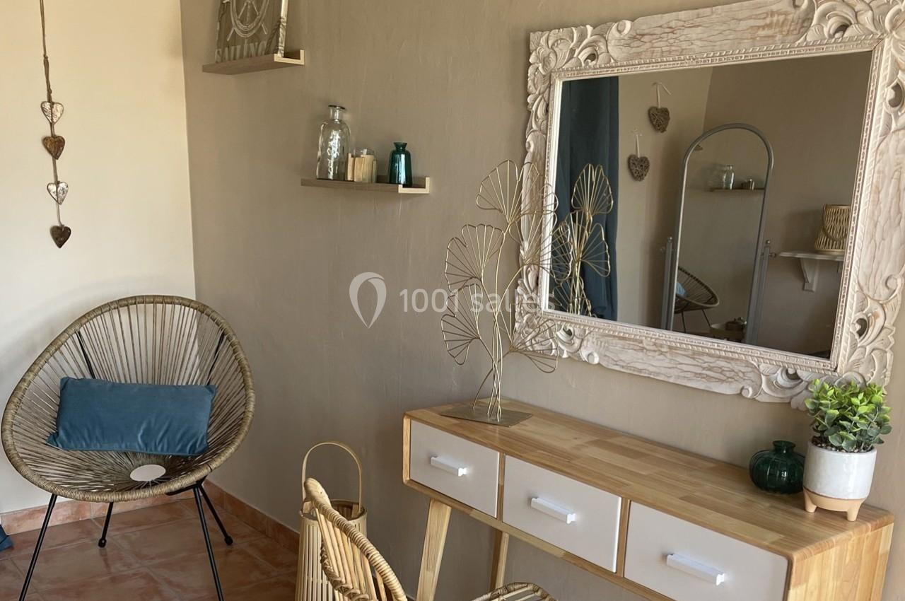Coin de décoration intérieure avec un miroir encadré, une console en bois, une chaise en rotin et des éléments décoratifs.
