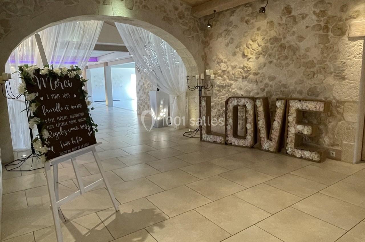 Salle de réception décorée avec un panneau de remerciement, des rideaux lumineux et des lettres ’LOVE’ illuminées.