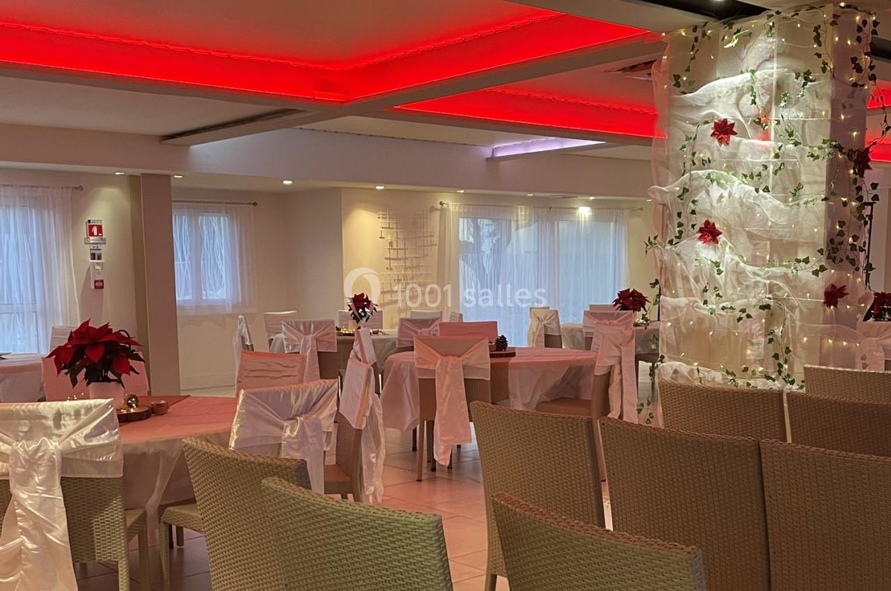 Salle de réception décorée avec des nappes blanches, des poinsettias rouges et un éclairage tamisé rouge au plafond.