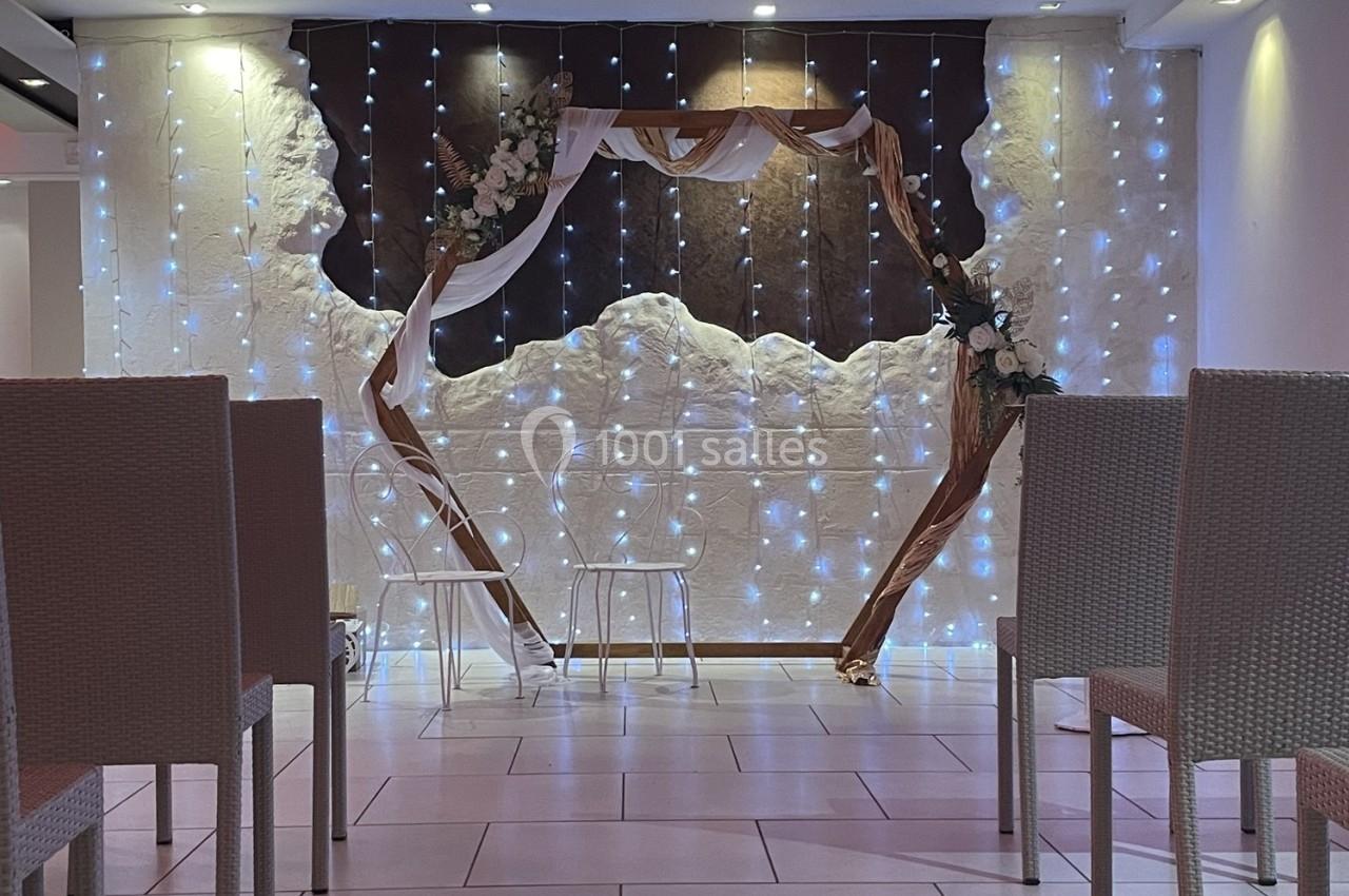 Arche décorative en bois ornée de fleurs et de voilages, entourée de guirlandes lumineuses dans une salle aménagée.