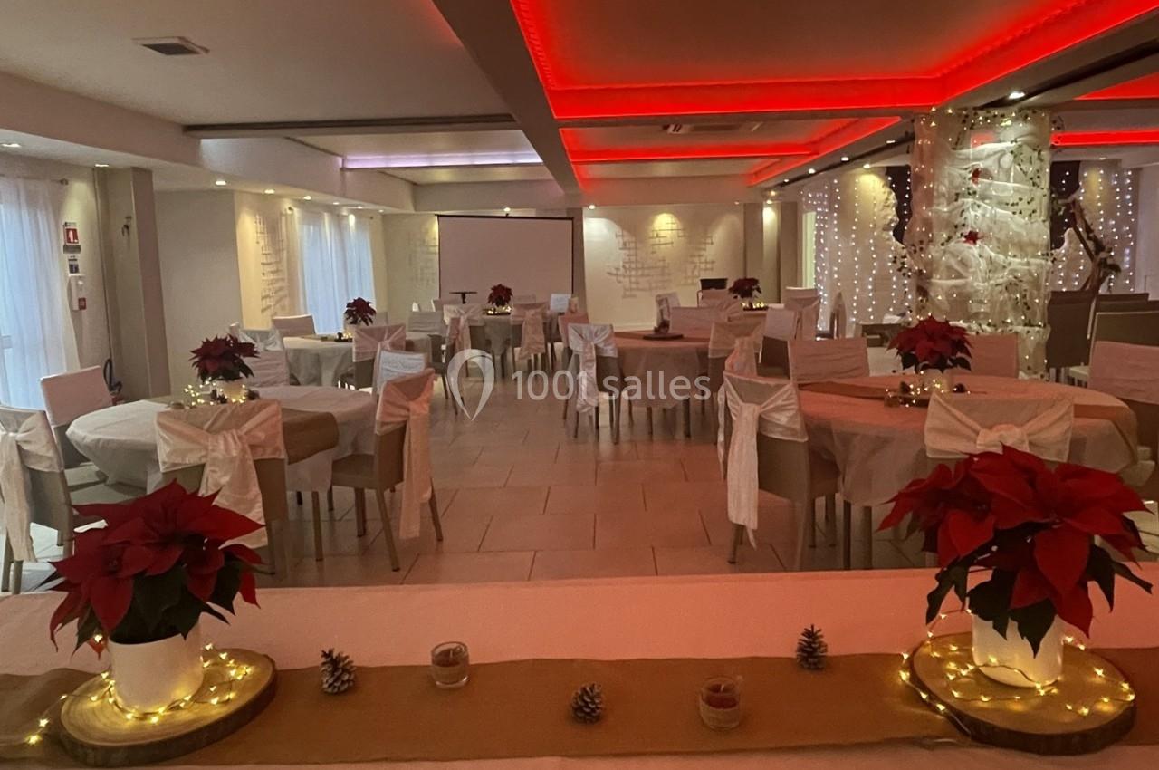 Salle de réception décorée pour les fêtes, avec tables rondes, nappes blanches, poinsettias et éclairage chaleureux.