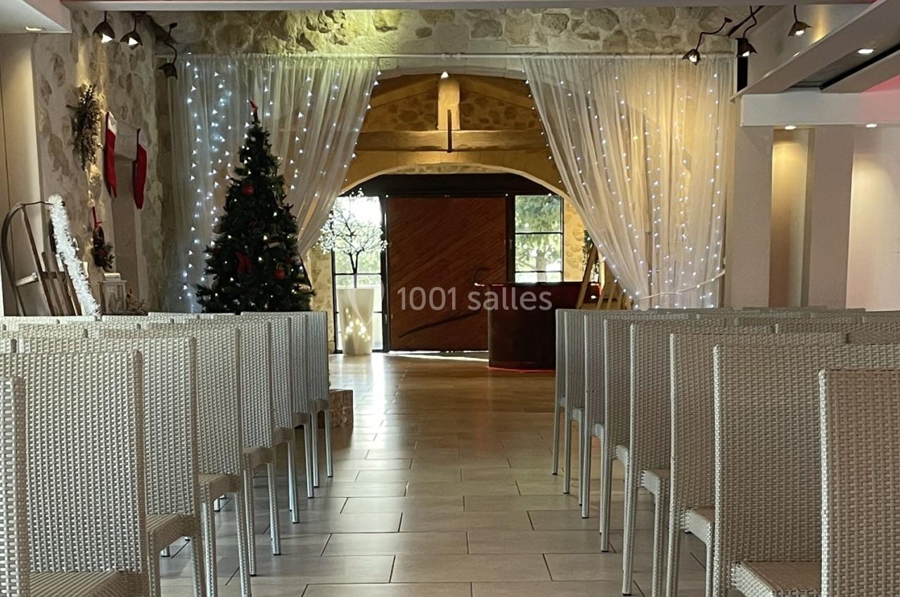 Salle décorée pour les fêtes avec un sapin de Noël, des guirlandes lumineuses et des chaises alignées face à une porte en…