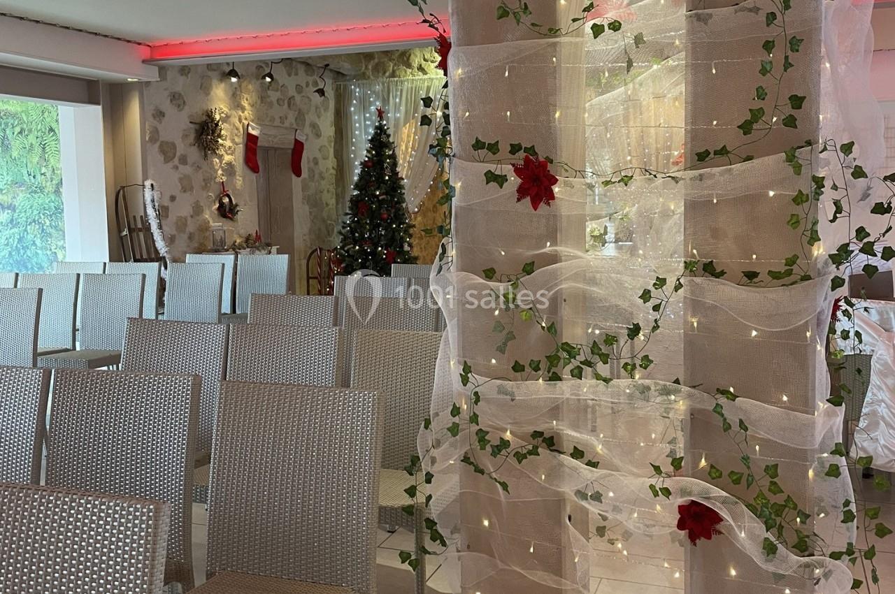 Salle décorée pour Noël avec des chaises alignées, un sapin illuminé et des guirlandes ornées de feuillage et de fleurs…