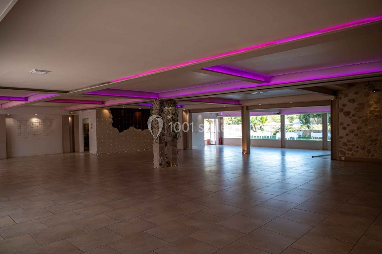 Salle spacieuse avec carrelage clair, éclairage LED violet au plafond et grandes baies vitrées donnant sur l'extérieur.