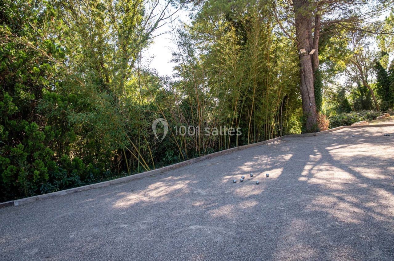 Terrain de pétanque ombragé entouré de bambous et d'arbres, avec des boules posées au sol.