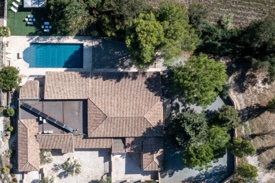 Vue aérienne d'une maison avec toit en tuiles, piscine rectangulaire et jardin arboré dans un cadre rural.
