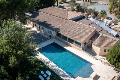 Vue aérienne d'une maison avec toit en tuiles, piscine rectangulaire et jardin arboré dans un cadre rural.