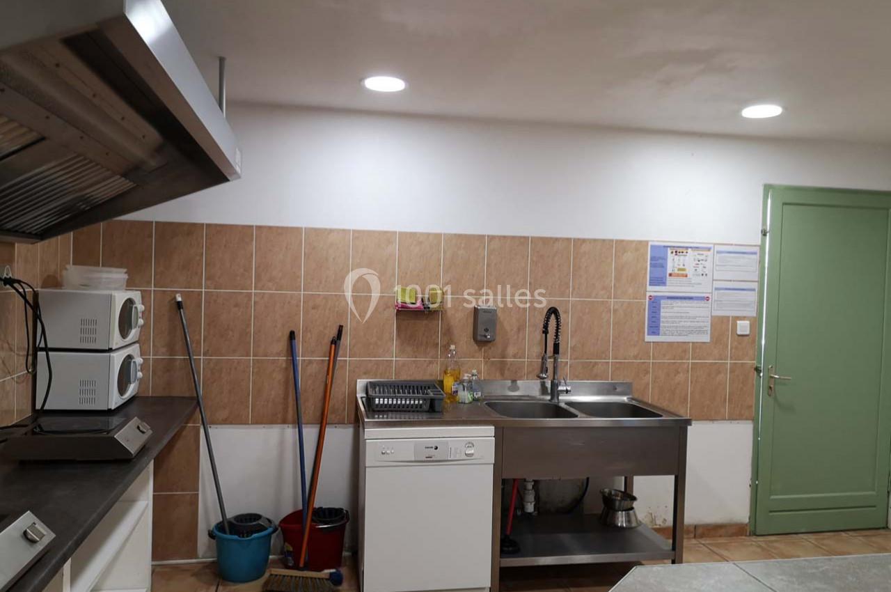 Cuisine équipée avec évier double, lave-vaisselle, micro-ondes, ustensiles de nettoyage et éclairage au plafond.