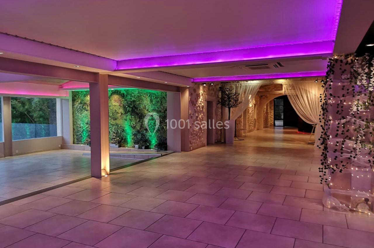 Salle spacieuse avec éclairage LED violet, murs végétalisés et rideaux blancs créant une ambiance élégante.