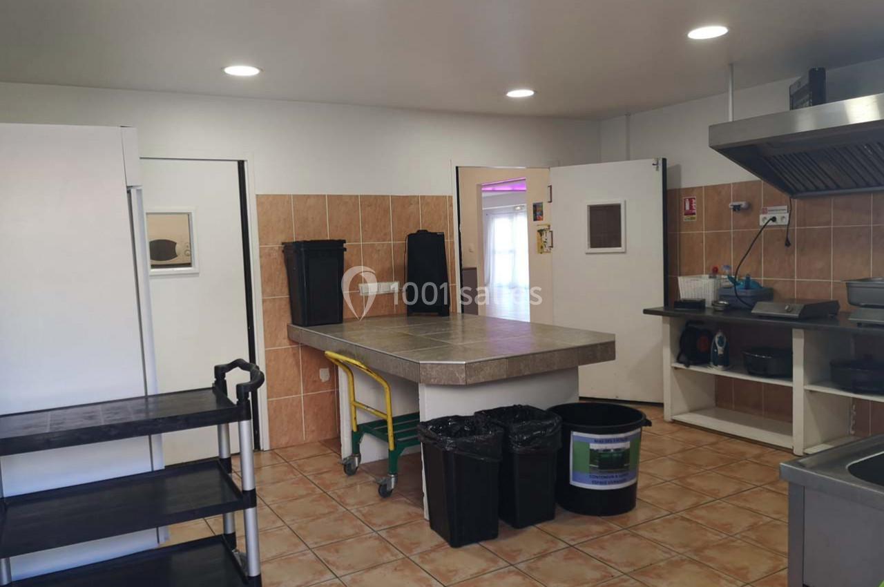 Cuisine professionnelle avec plan de travail central, étagère roulante, poubelles et équipements de cuisson.