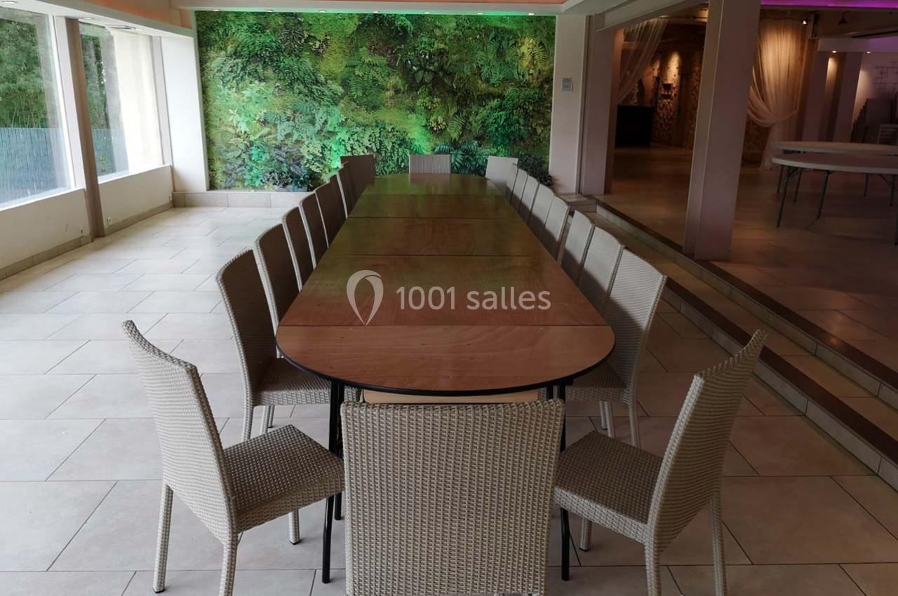 Table rectangulaire en bois entourée de chaises en rotin dans une salle lumineuse avec un mur végétal en arrière-plan.