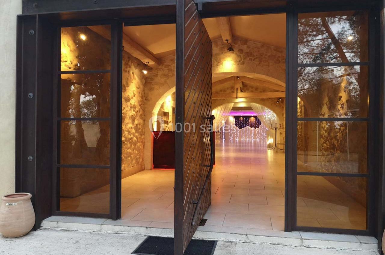 Entrée ouverte d'un bâtiment en pierre avec porte en bois et vue sur un intérieur éclairé et décoré.