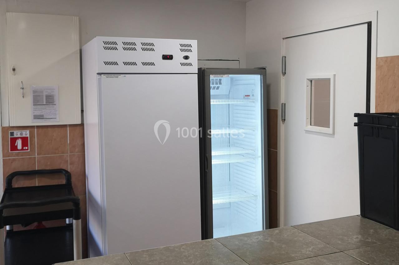 Deux réfrigérateurs, dont un ouvert, dans une pièce carrelée avec une poubelle et une porte blanche.