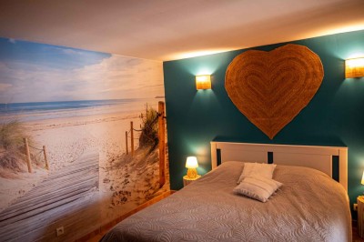 Chambre avec un lit double, mur décoré d'une photo de plage et éclairage doux avec appliques et lampes de chevet.