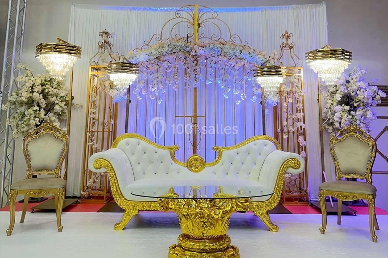 Canapé doré avec table assortie, entouré de chaises et décoré de fleurs blanches sous des lustres élégants.